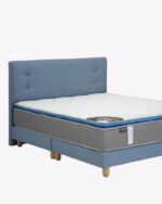 close up shot of wooden legs blue fabric bed frame with mattress